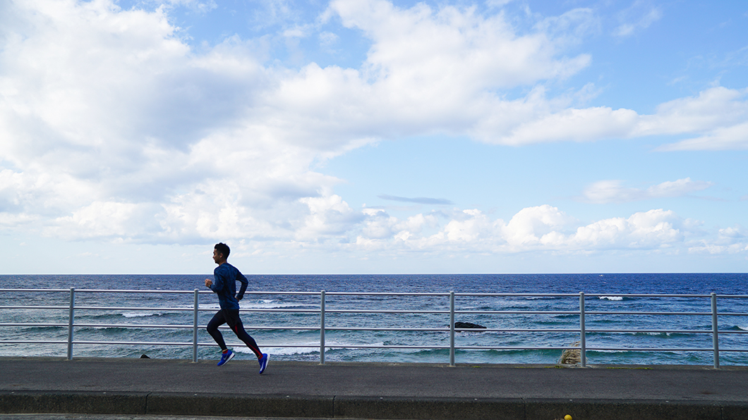 奄美市笠利海沿いを走る男性